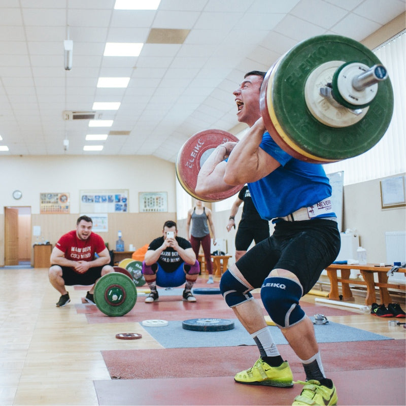 Person lifting a barbell in a weightlifting gym with other people in the background.