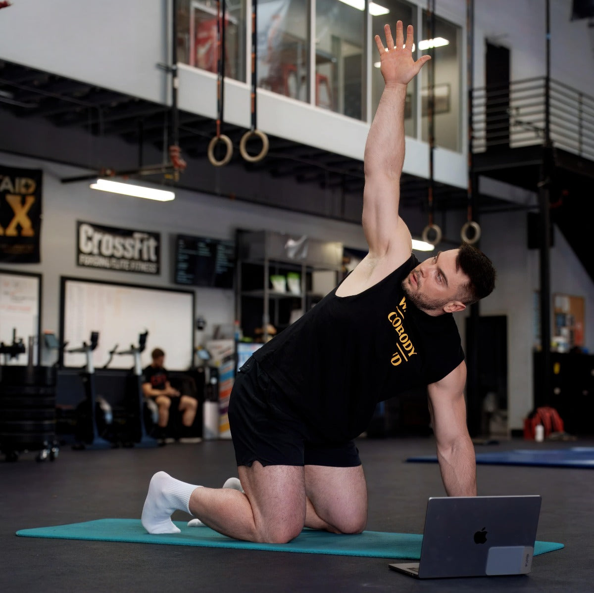 Person exercising on a mat with a laptop in a gym setting (Torokhtiy Weightlifting)