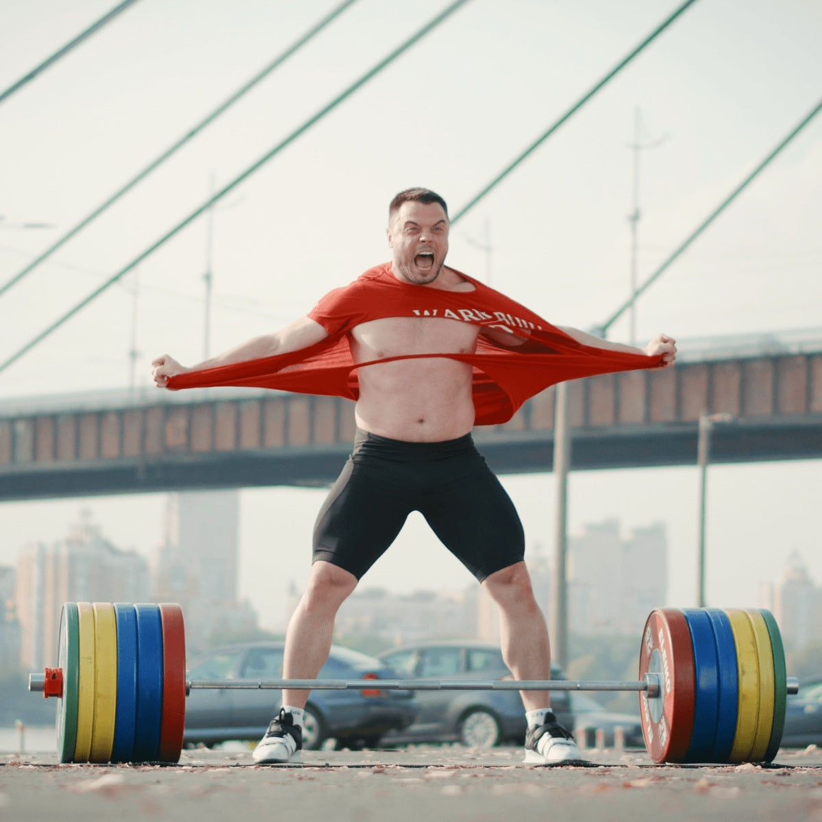 Man lifting a barbell outdoors with a bridge in the background (Torokhtiy Weightlifting)