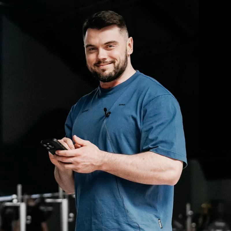 Man in a blue shirt holding a phone against a dark background (Torokhtiy Weightlifting)