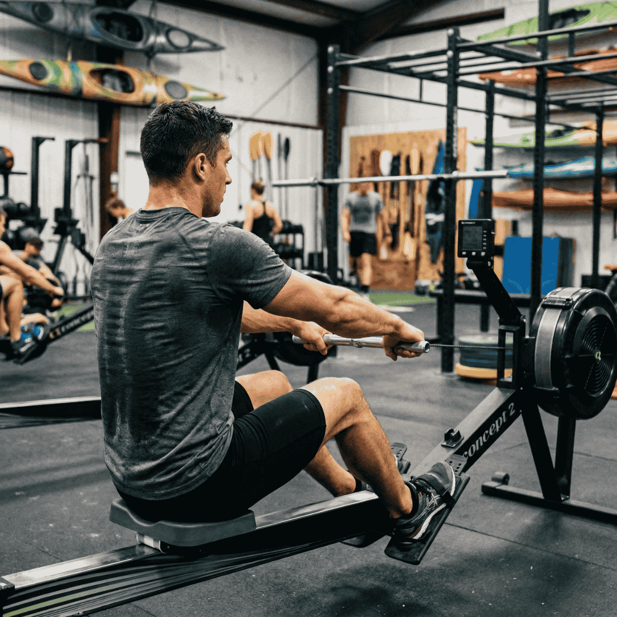 Man using a rowing machine in a gym setting with various equipment in the background.